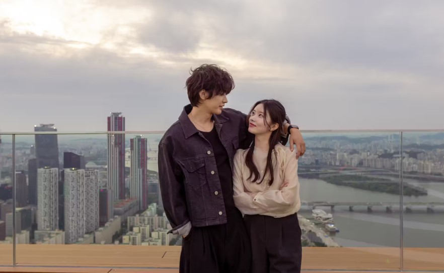 Couple standing on an open-air rooftop terrace with glass railings above the Han River and Seoul high-rises