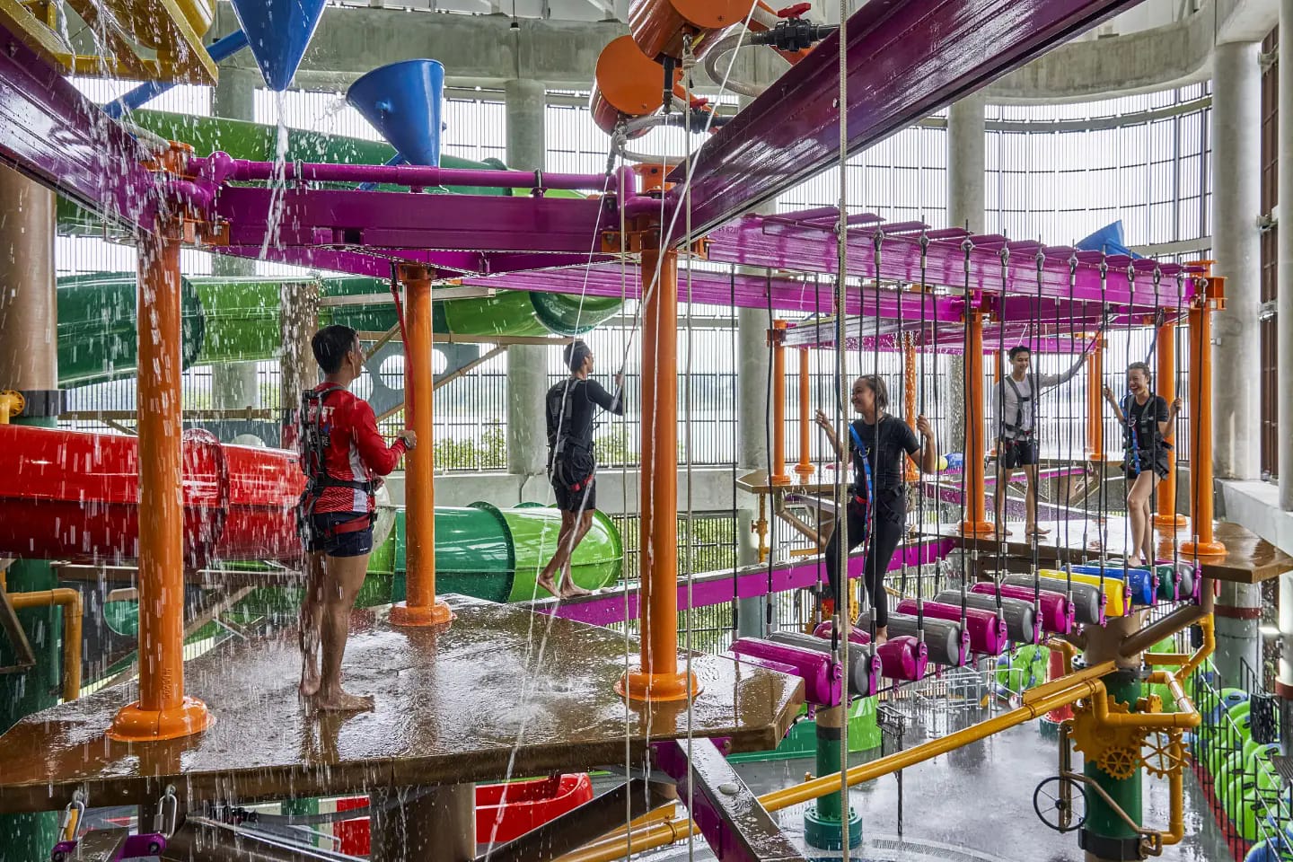 Harnessed visitors crossing a ropes course above water slides at Aqua Adventure