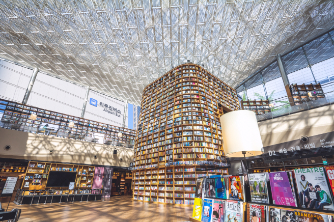 Tall curved wooden bookshelves filled with books under the glass roof of Starfield Library in COEX Mall