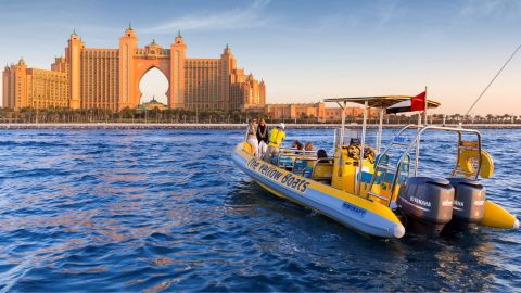 Yellow speedboat with passengers in front of Atlantis The Palm in golden late-afternoon light
