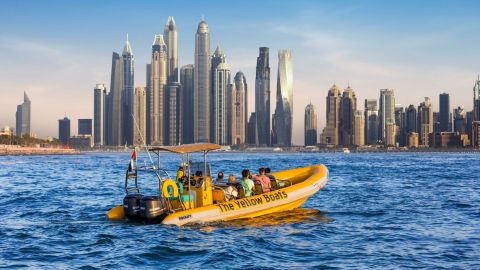 Yellow speedboat carrying passengers on the water with the Dubai Marina skyline behind