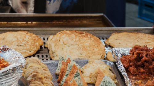 Golden mung bean pancakes and fried snacks laid out on metal trays at a Gwangjang Market food stall